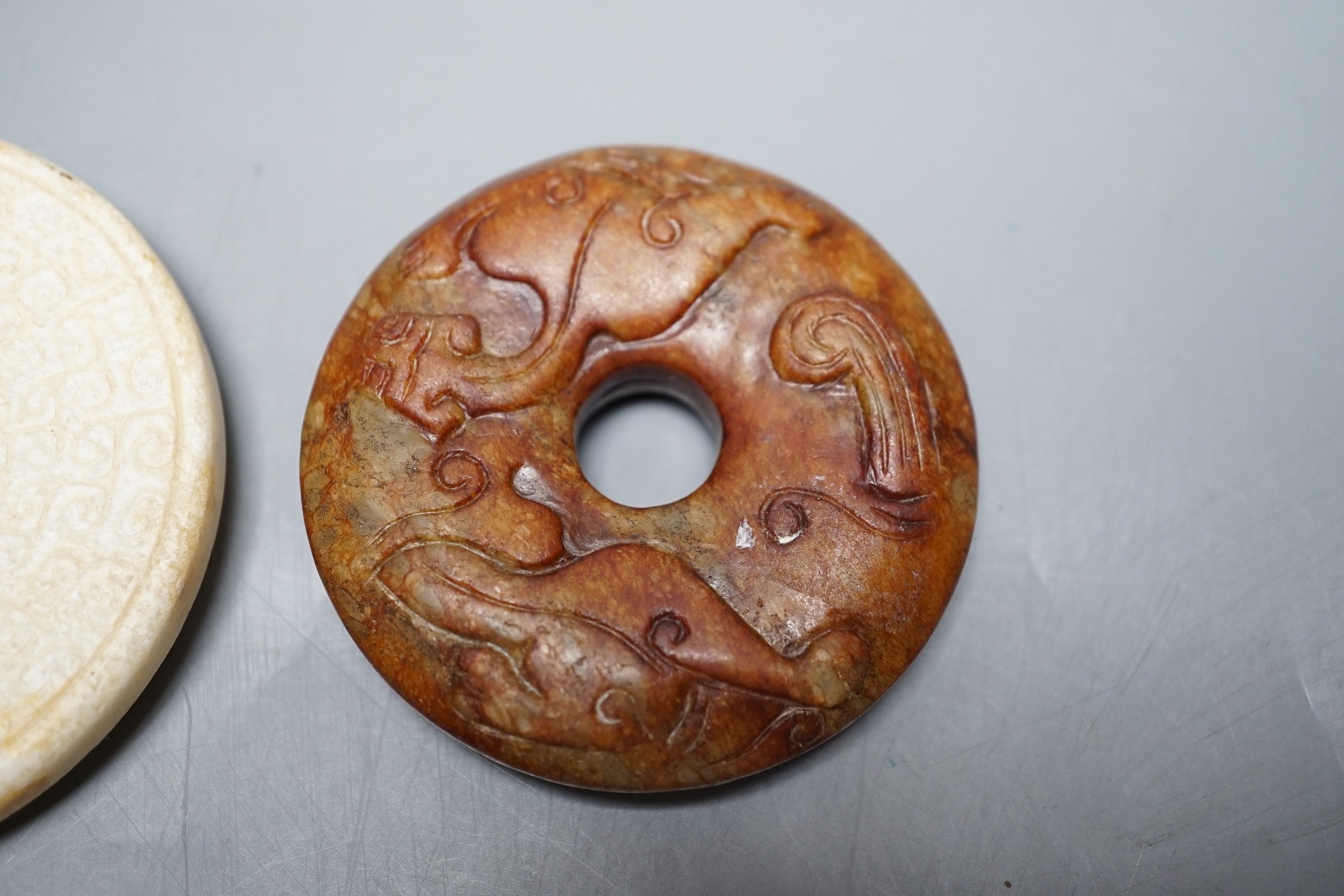 A Chinese green jade 'cash' pendant, a russet jade bi-disc and a burnt jade circular plaque